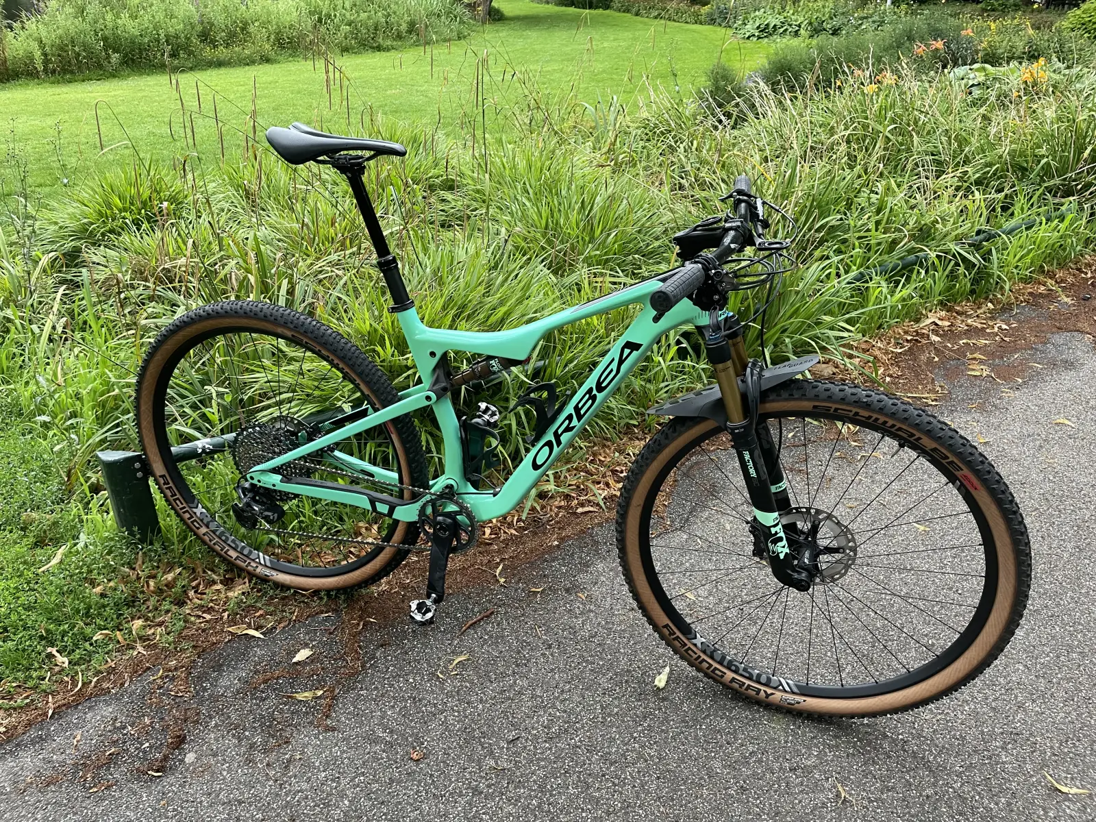 Orbea full-suspension MTB in factory celeste green, full bike on a path beside grass